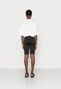 T-shirt branco curto com ombros caídos, combinado com calções justos pretos até ao joelho. Sandálias de plataforma pretas completam o visual.