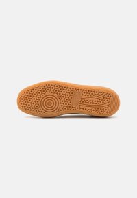 Semelle de chaussure avec motifs de bande de roulement circulaires et linéaires, présentant un logo de marque embossé près de la voûte plantaire, sur un fond uni.