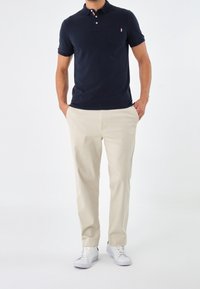 Námornícky modré polo tričko s třemi knoflíky a náprsní kapsou, spárované s krémovými kalhotami. Nošeno s bílými teniskami.