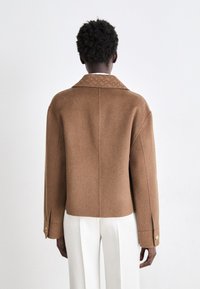 Veste en laine mélangée marron avec un design structuré, un large col et des fentes latérales. Présente des poignets boutonnés et une texture lisse.