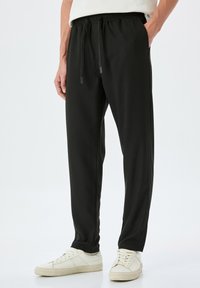 Zwarte sportbroek met een relaxte pasvorm, elastische tailleband en verstelbare koordjes. Glad stof met zijzakken en taps toelopende pijpen.
