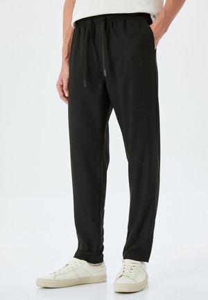Schwarze Sporthose mit lockerer Passform, elastischem Bund und verstellbaren Kordelzügen. Glattes Material mit Seitentaschen und schmal zulaufenden Beinen.