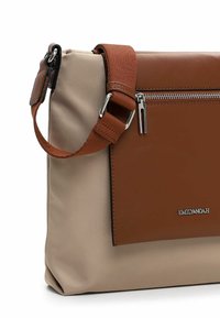 Sac en cuir brun et tissu beige avec une poche frontale zippée, une bandoulière réglable et des accents en métal argenté.