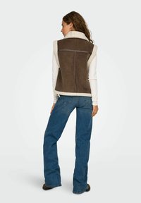 Brun kordfløjsp vest med creme fleecekrave og kant, prydet med en sømløs bagside og en generelt afslappet pasform, parret med bredde jeans i blå.
