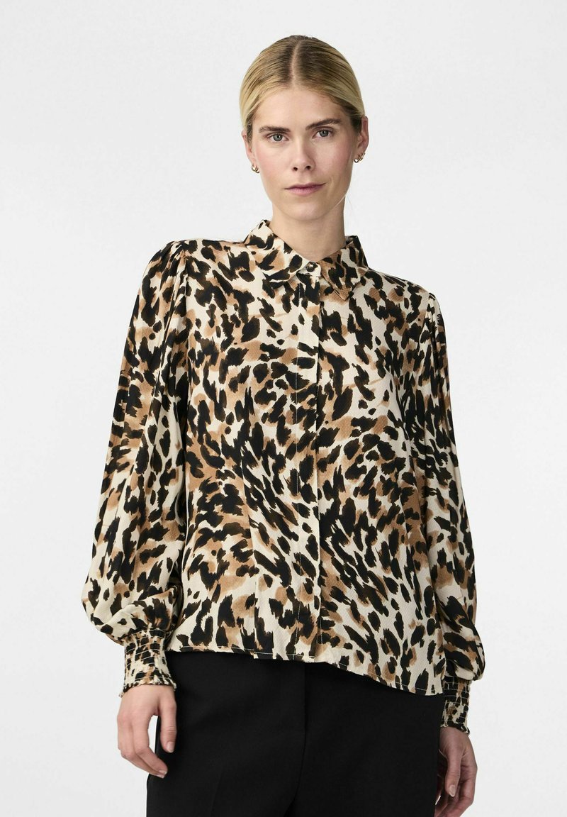 Leeuwenspots blouse in beige, bruin en zwart; heeft een klassieke kraag, lange puffmouwen en een knoopsluiting aan de voorkant. Soepele, lichte stof.