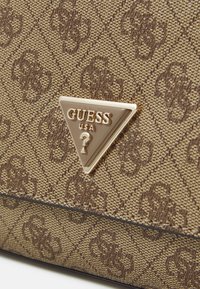 Sac à main synthétique marron avec une surface texturée tissée, présentant une plaque logo triangulaire dorée et un motif subtil dans une teinte plus claire.