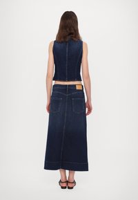 Denim vest with a fitted design and dark blue color, paired with a long, dark blue denim skirt featuring two back pockets.