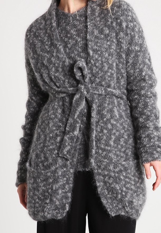 Šedý pletený cardigan s volným střihem, předním zavíráním na uzel a texturovanou, huňatou látkou. Obsahuje otevřený přední díl a dvě boční kapsy.