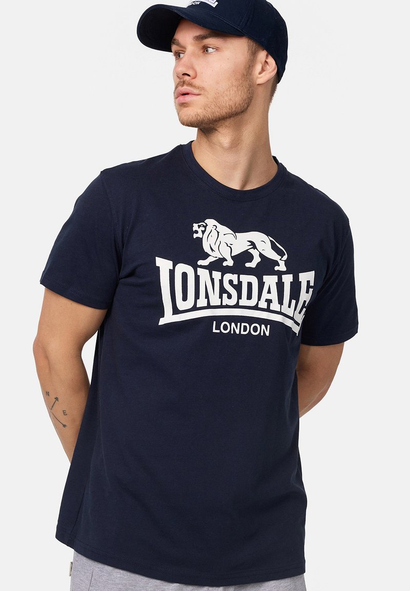 Tricou din bumbac bleu marin cu un grafic alb al unui leu și textul "Lonsdale London". Mâneci scurte și un design clasic cu guler rotund.