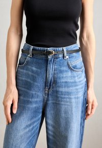 Un débardeur noir à côtes associé à un jean en denim bleu clair. Une ceinture noire fine avec une boucle dorée accentue la taille.