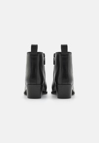 Botas de couro pretas até ao tornozelo com bico arredondado, salto bloco de altura média e fecho lateral. Design minimalista com um laço na parte de trás.