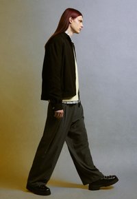 Fekete külső dzseki, világos sárga pulóver, fehér galléros ing, szürke csíkos bő nadrág és fekete platform cipő. Hosszú vörös haj.