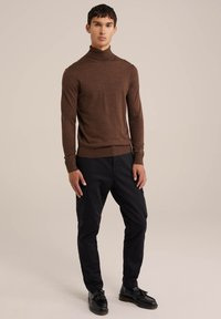 Rjava, dolgosleeve turtleneck pletenina iz mehkega materiala; v kombinaciji s črnimi tovorni hlačami in črnimi čevlji z dekorativnim robom.