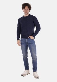 Maglione a collo alto blu navy a maglia con polsini e orlo a costine, abbinato a jeans slim-fit azzurri e sneakers bianche con dettagli neri.