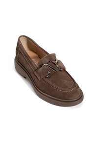 Mocassin marron en daim avec semelle épaisse en caoutchouc et ornement métallique argenté décoratif sur le dessus, présenté sous un léger angle sur fond blanc.