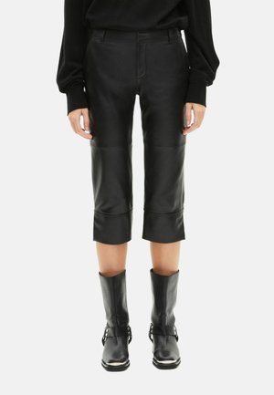 Zwarte leren cropped broek met een aansluitend ontwerp en omgeslagen zoom, gecombineerd met zwarte leren enkellaarzen met gespen.