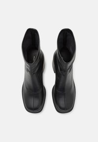 Stivali alla caviglia in pelle nera con una texture liscia, punte quadrate e un design minimalista. Presentano cuciture sottili e una suola nera sottile.