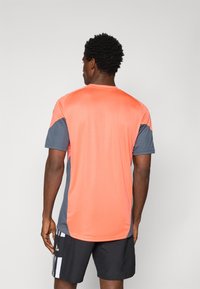 Korte mouwen sportshirt in levendig koraal met grijze accenten. Gemaakt van soepel, lichtgewicht stof, het heeft contrasterende panelen aan de zijkanten.