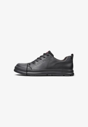 Black leather sneaker with smooth texture, rounded toe, five eyelets, and thick rubber sole. Minimalist design with subtle branding on the side.