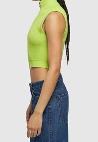 Top corto acanalado verde con cuello alto y diseño sin mangas, combinado con una falda de mezclilla de cintura alta. Textura suave y forma ajustada.