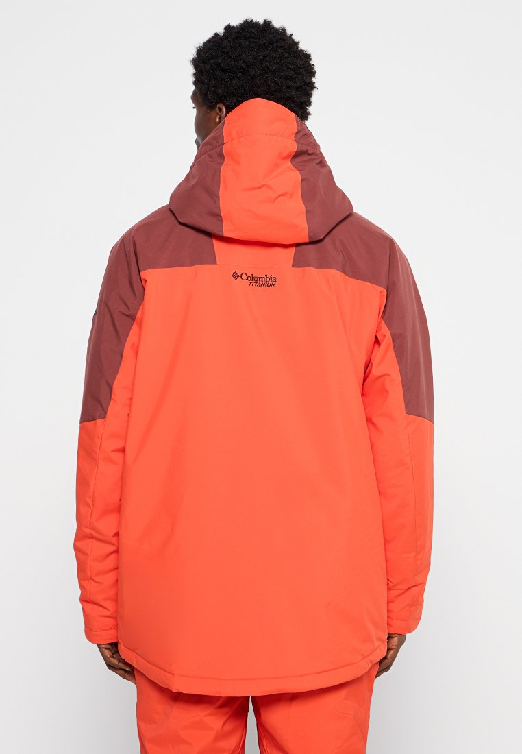 Person, die eine zweifarbige orange-braune Columbia Titanium Kapuzenjacke trägt, von hinten vor einem schlichten weißen Hintergrund gezeigt.