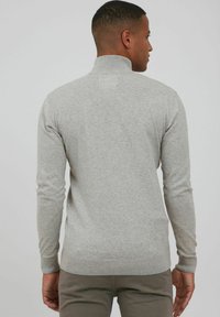 Suéter gris de punto con un cuello alto y mangas largas. Presenta puños y dobladillo acanalados, además de una textura suave y lisa.