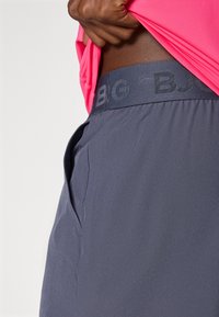 Γκρι αθλητικοί σορτς με υφασμάτινη ζώνη που παρουσιάζει διακριτική σήμανση. �Τα σορτς διαθέτουν πλαϊνές τσέπες και ελαφρύ, λείο ύφασμα.