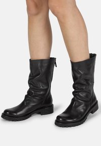 Botas de cuero negras hasta el tobillo con un diseño arrugado, superficie texturizada y una suela negra resistente con un ligero tacón y cierre de cremallera.
