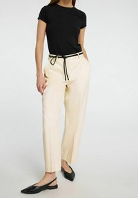 Svart t-shirt med kort ärm, matchad med krämfärgade byxor med svart dragsko. Bärs med svarta slingback-skor. Slät tygtextur.