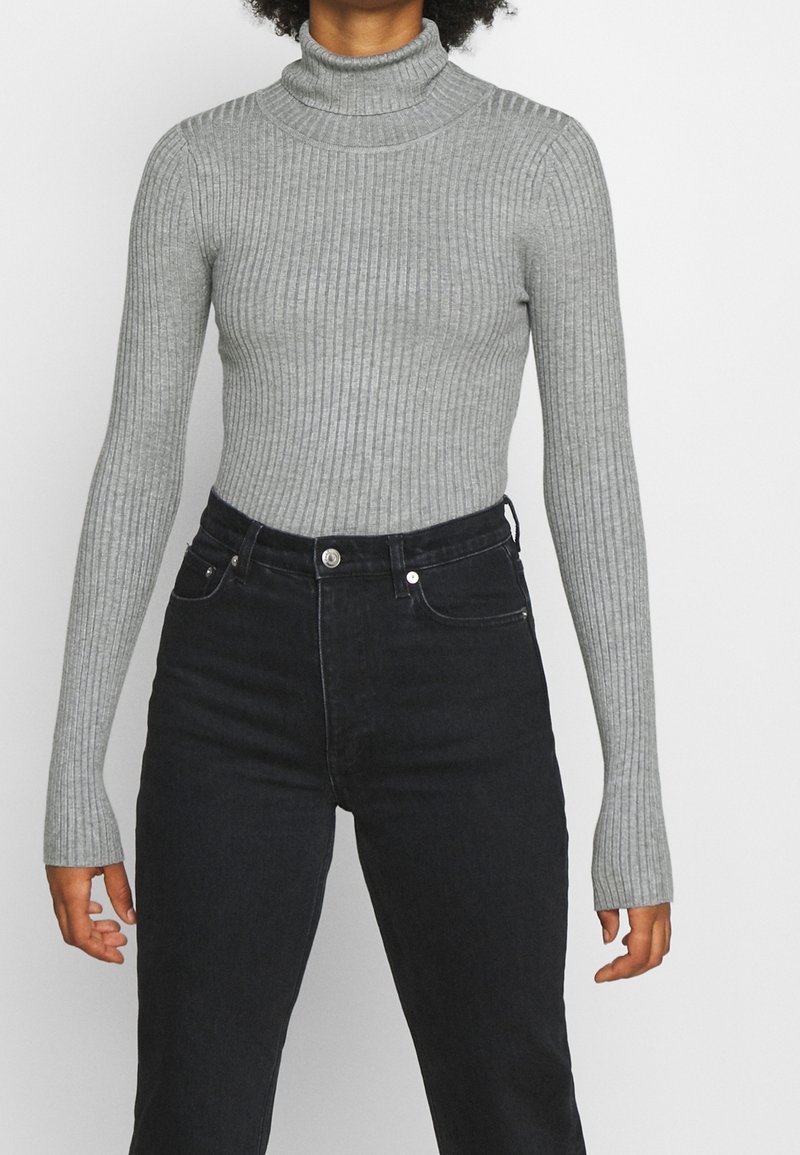 Maglione grigio a coste con collo alto e maniche lunghe, caratterizzato da un design aderente e un tessuto testurizzato, abbinato a jeans neri in denim a vita alta.