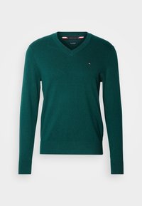 Pull vert foncé à manches longues avec col en V et petit logo multicolore sur le côté gauche de la poitrine, présenté sur un fond blanc.