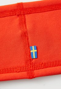 Close-up of red fabric with reinforced stitching and a small blue and yellow Swedish flag tag sewn into the seam.