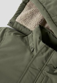 Giacca invernale verde oliva con colletto alto, bottoni a scatto e foderatura in pile beige all'interno del cappuccio.