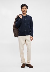 Ναυτικό πουλόβερ με κουμπιά και γιακά, με τσέπη στο στήθος, σε συνδυασμό με κρεμ παντελόνι και καφέ μποτάκια μέχρι τον αστράγαλο.