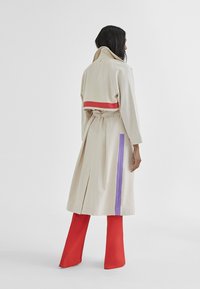 Beżowy trenchcoat z czerwonymi i purpurowymi akcentami, z pasem w talii i rozcięciem z tyłu. Połączony z czerwonymi spodniami dzwonowymi.