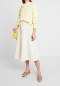 Żółty sweter w prążki, biała koszula z kołnierzykiem, kremowa spódnica midi, beżowe espadryle oraz mała neonowożółta torebka na ramię.