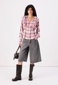 Pink and blue checked blouse with ruffled accents, paired with gray wide-leg shorts and brown knee-high boots with buckles.