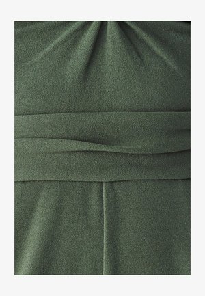 Tamnozelena haljina s teksturiranim materijalom, nabranim detaljem na bustu, horizontalnim plisiranjima i uskim pojasom.