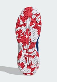 Semelle de sneaker blanche et rouge avec un motif texturé, comportant des rainures de traction prononcées et un accent bleu sur le côté.