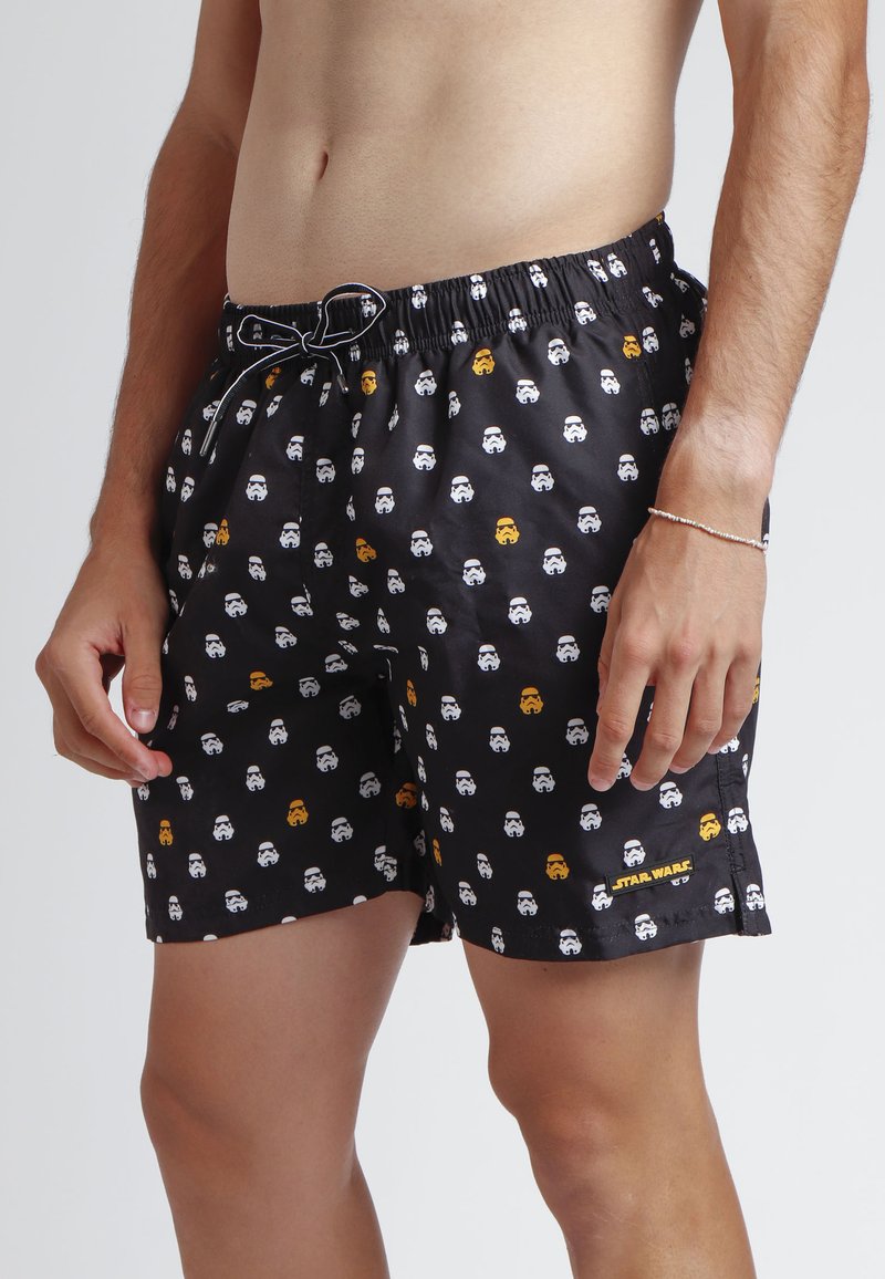 Bañador negro con un patrón repetitivo de caras estilizadas en blanco y naranja. Cintura elástica con cordón; logo de la marca en el dobladillo.