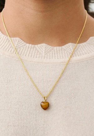 Gold chain necklace with a small heart-shaped amber pendant worn over a cream knitted sweater with a scalloped neckline.