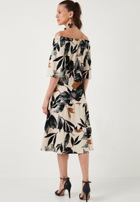 Off-the-shoulder dress with a floral pattern in black, cream, and brown. Flared sleeves, tiered design, and ankle-strap heels. Textured fabric.