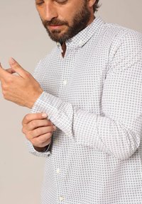 Witte button-up shirt met een geometrisch zwart patroon, lange mouwen en een kraag, gemaakt van een lichte stof met een gladde textuur.