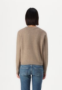 Sweater de malha bege com decote redondo, mangas longas e barra canelada. Usado com jeans de denim azuis com bolsos traseiros padrão.