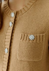 Brauner Strickcardigan mit Rundhalsausschnitt, dekorativen Kristallknöpfen und einer aufgesetzten Tasche mit einem floralem Kristallakzent.