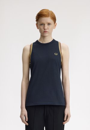 Giovane con capelli corti rossi, indossa una maglia senza maniche blu navy con strisce gialle e un piccolo logo di alloro giallo, in piedi davanti a uno sfondo semplice.