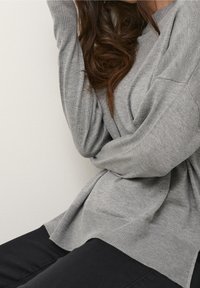 Maglione lavorato a maglia di colore grigio chiaro con una vestibilità comoda, polsini a coste e scollo arrotondato. Abbinato a pantaloni neri, che mettono in risalto una texture morbida.