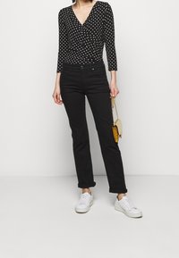 Musta pitkähihaista toppia valkoisilla pilkuilla, yhdistettynä korkeavyötäröisiin mustiin farkkuihin ja valkoisiin lenkkareihin. Pitelee pientä kultaista käsilaukkua.