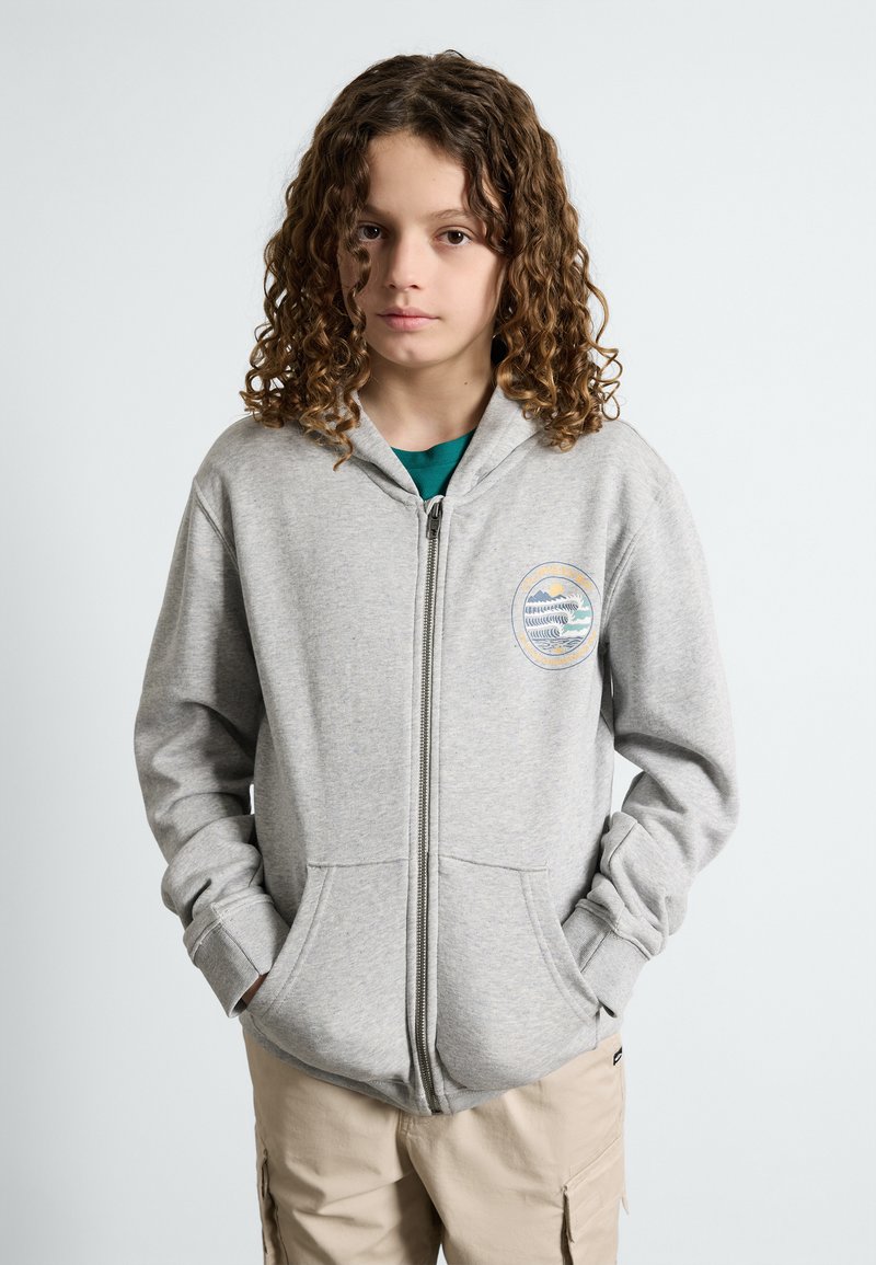 Moleton cinza com fecho, feito de uma mistura de algodão, apresentando um bolso frontal e um logotipo circular no lado esquerdo do peito. Mangas longas com punhos canelados.