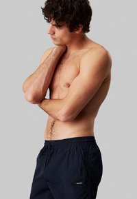 Costumi da bagno blu navy con vita regolabile e tasche. Realizzati in materiale leggero, presentano una patch con il logo Calvin Klein sul lato.